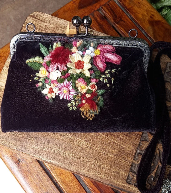 A chic velvet handcrafted handbag featuring hand embroidered vibrant flowers, combining sophistication with a touch of nature-inspired beauty.