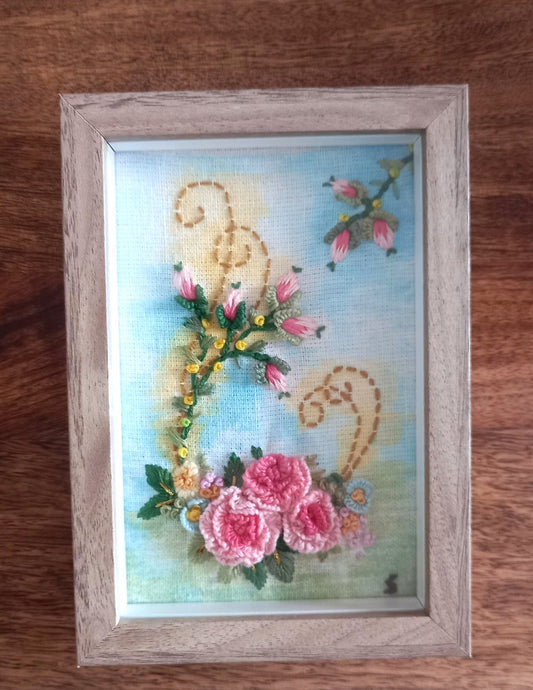 Delicate pink roses with rose buds embroidered on a lightly painted background to beautify home or workspace mounted in a modern frame.