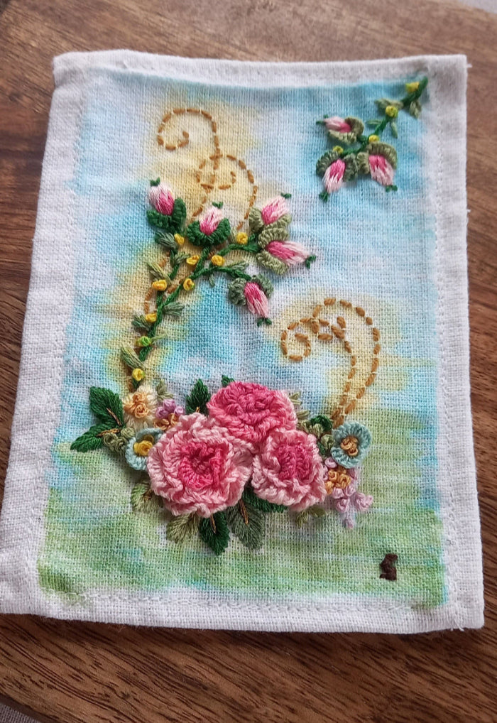 Delicate embroidered pink roses with rose buds on a lightly painted background to beautify home or workspace mounted in a modern frame.