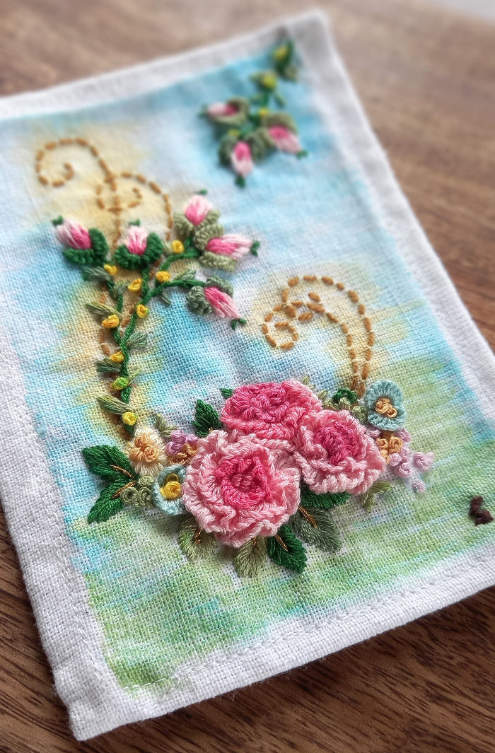 Delicate embroidered pink roses with rose buds on a lightly painted background to beautify home or workspace mounted in a modern frame.