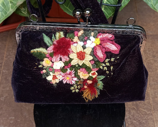 An elegant velvet purse with hand embroidered floral designs, reflecting a harmonious blend of style and artistic flair. Colorful 3d style flowers and leaves.