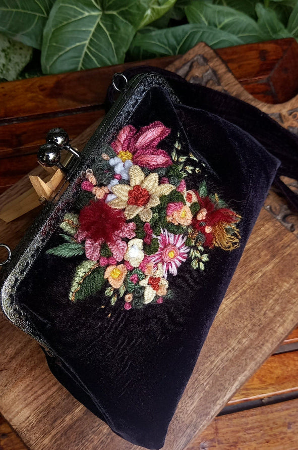 A stylish velvet purse adorned with hand embroidered colorful flowers, perfect for adding a touch of charm to any outfit.