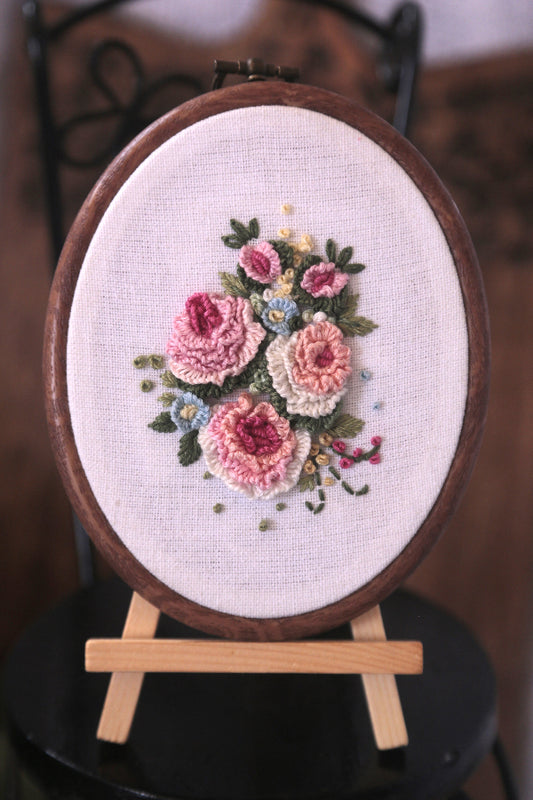 Embroidery art displaying three pastel peach roses elegantly stitched on a oval hoop canvas.