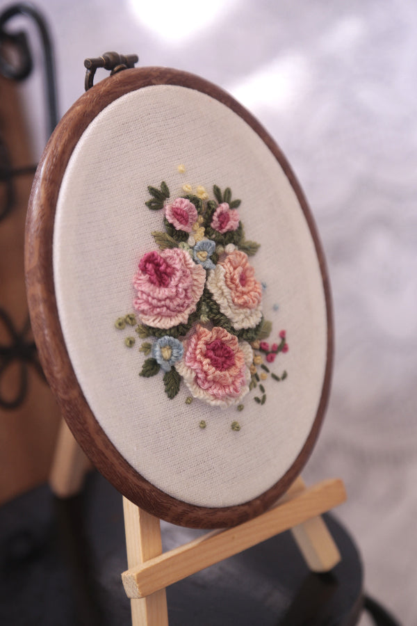 Close-up of hoop art featuring delicate embroidery of three pastel peach roses with green leaves in a Vintage style.