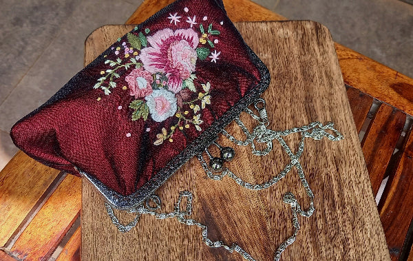 Velvet handcrafted purse with hand embroidered serene pastel peach flowers. The purse is featured on a wooden background 