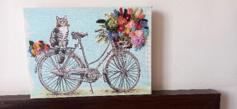 Canvas with a printed black and white cat sitting on a cycle with a hand embroidered bouquet of flowers