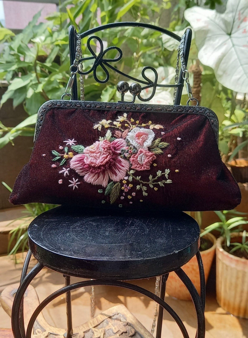 Velvet handcrafted purse with hand embroidered serene pastel peach flowers on a mini chair in greenery. 