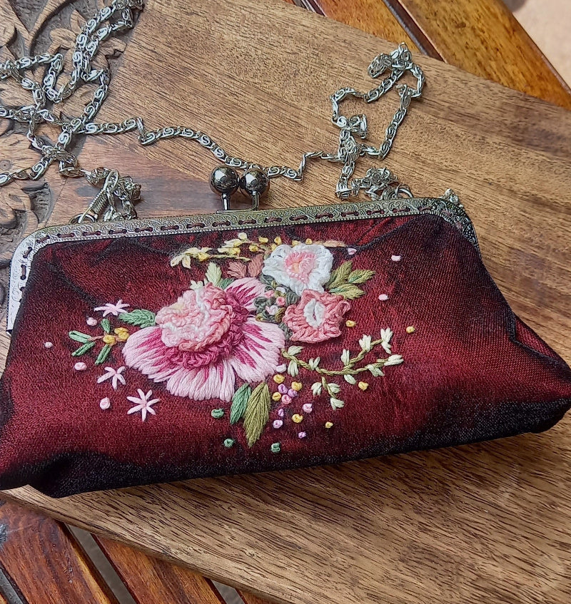 Velvet handcrafted purse with hand embroidered serene pastel peach flowers on a mini chair in greenery. 