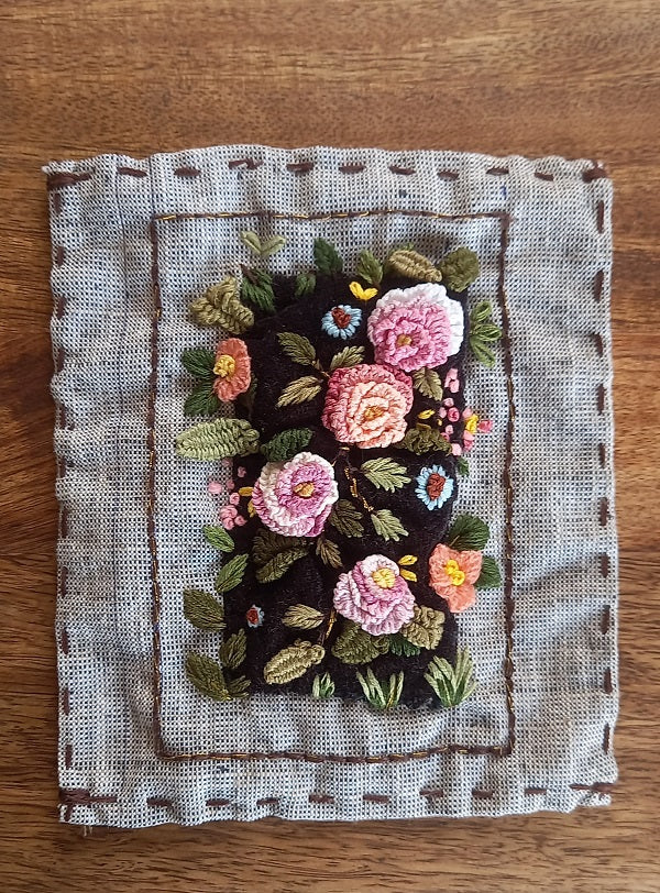 Delicate artistic hand embroidered textile art of 3D roses in pink and pastel colors and greenery on velvet background and mounted on khadi linen fabric. 