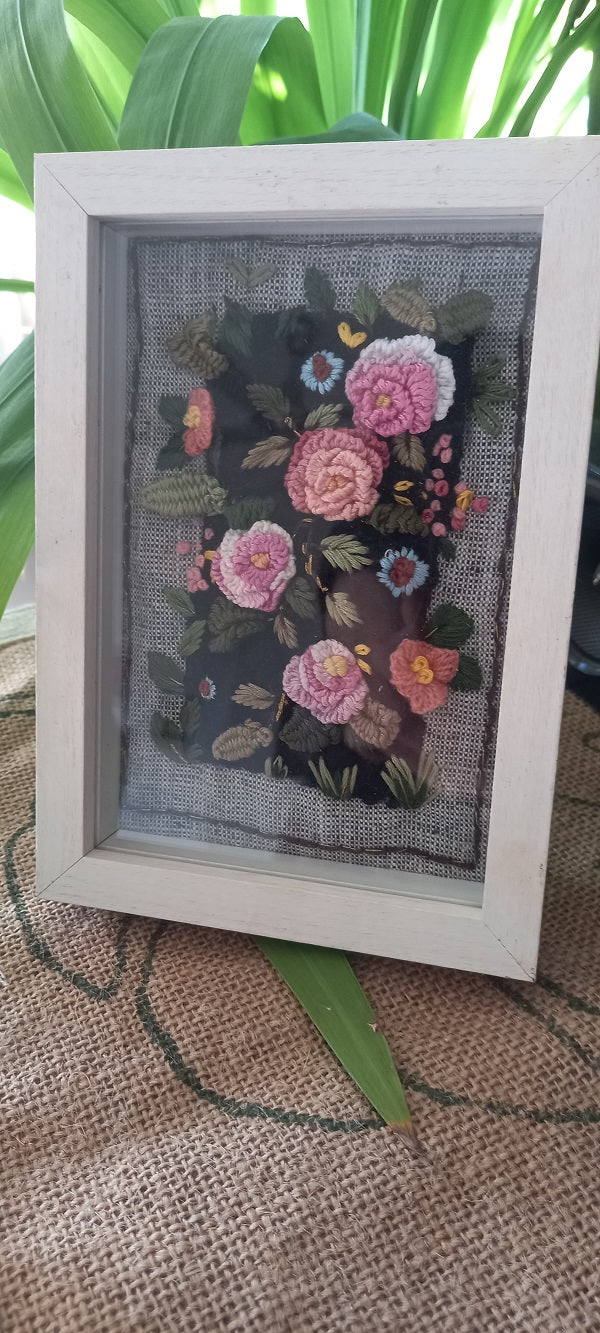 Delicate artistic hand embroidered 3D roses in pink and pastel colors and greenery on velvet background and mounted on khadi linen fabric. The artwork is placed in a beautiful box frame.  