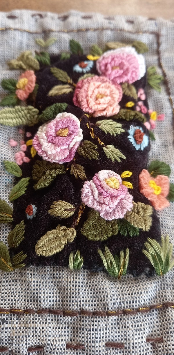 Delicate artistic hand embroidered textile art 3D roses in pink and pastel colors and greenery on velvet background and mounted on khadi linen fabric. The artwork is placed in a beautiful frame box.  