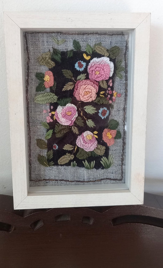 Delicate artistic hand embroidered textile art 3D roses in pink and pastel colors and leaves on velvet background and mounted on khadi linen fabric. The artwork is placed in a beautiful white colored box frame.  Front View.